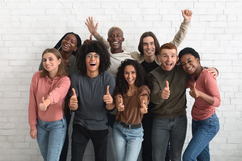 A group of multicultural individuals give thumbs up with big smiles.