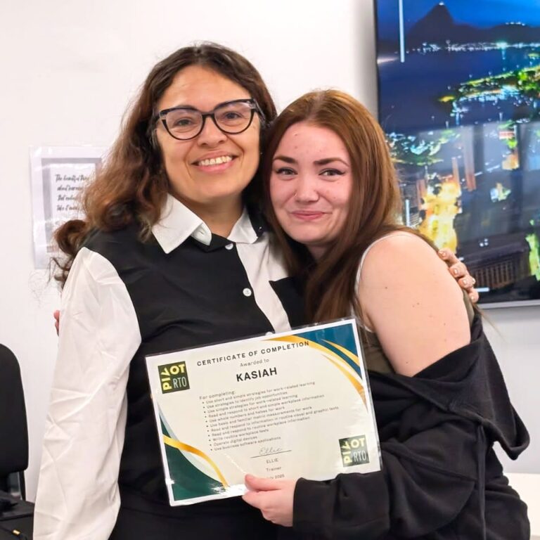 Kasiah smiles as she hugs her trainer Ellie while holding her Certificate I in Skills for Vocational Pathways, marking her achievement in the Skills for Education and Employment Program (SEE program) and her progress in learning for employment whilst exploring Australian career pathways.