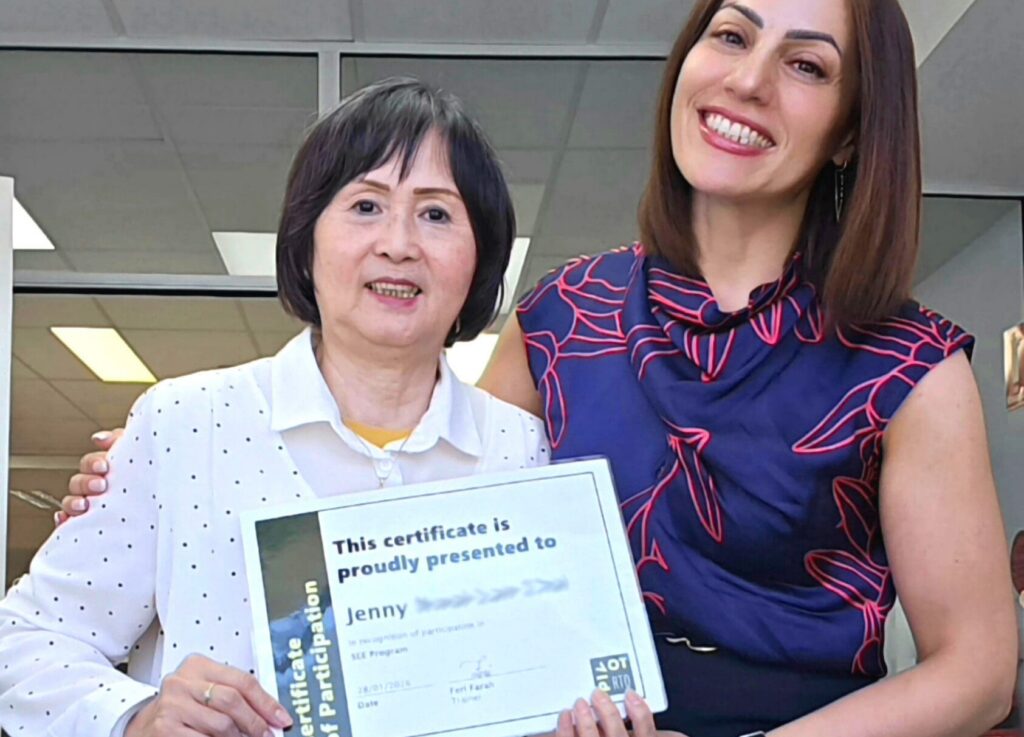 Jenny proudly holds her certificate beside her trainer after completing work ready training through the SEE program.