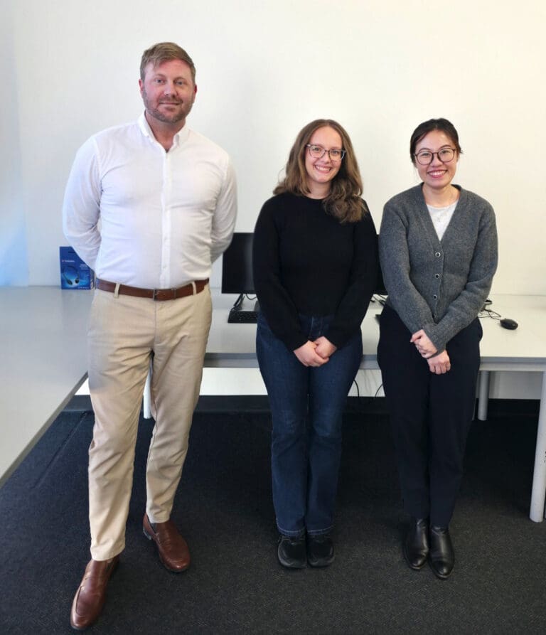 Three people standing in a training workspace, representing Vocational Education and Training focused on practical, work ready training.