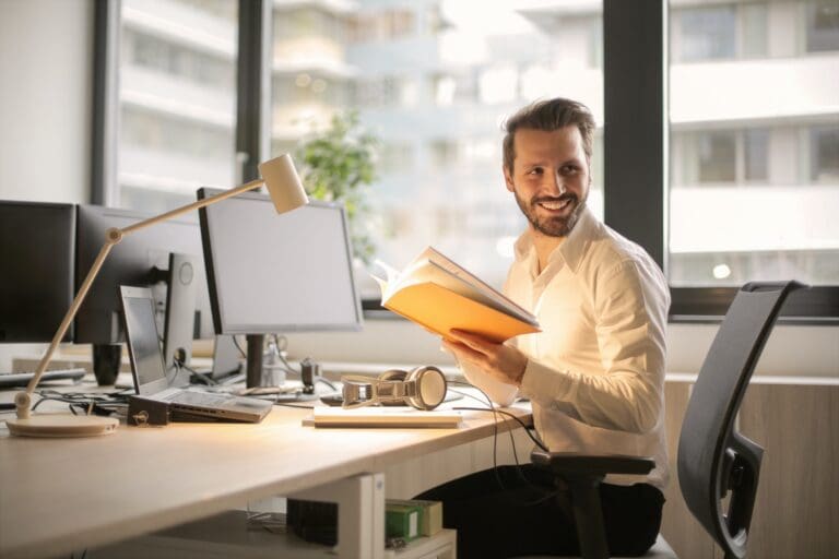 Person seated at a desk in an office reading training material, representing ongoing professional development through upskilled courses.