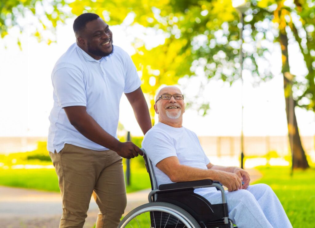 Person supporting an older adult using a wheelchair in an outdoor setting, representing a disability support worker role and learning for employment.